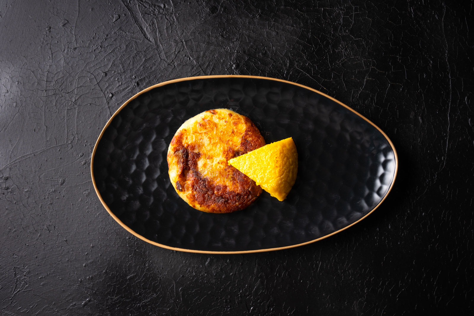 Italie du Nord Est shutterstock 2271126983 ©phld luca assiette de vue de dessus avec frico et polenta. plat typique du frioul. sur fond noir